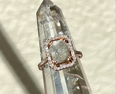 reamy gray rose-cut diamond with a delicate diamond halo and side diamond accents with two bezel hidden diamonds. The center diamond is set with double prongs for extra security all in 14-karat rose gold